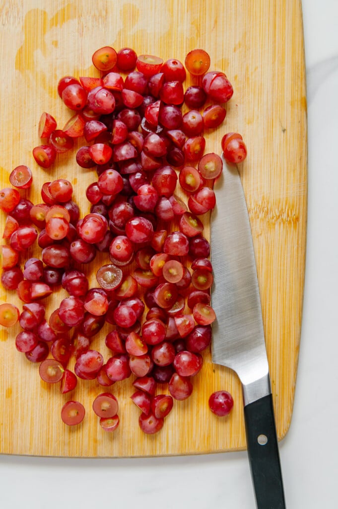 Halved red grapes on a wooden cutting board with a sharp knife.