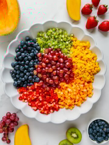 Finely chopped fresh fruit in a white bowl prior to being tossed together with a white background.