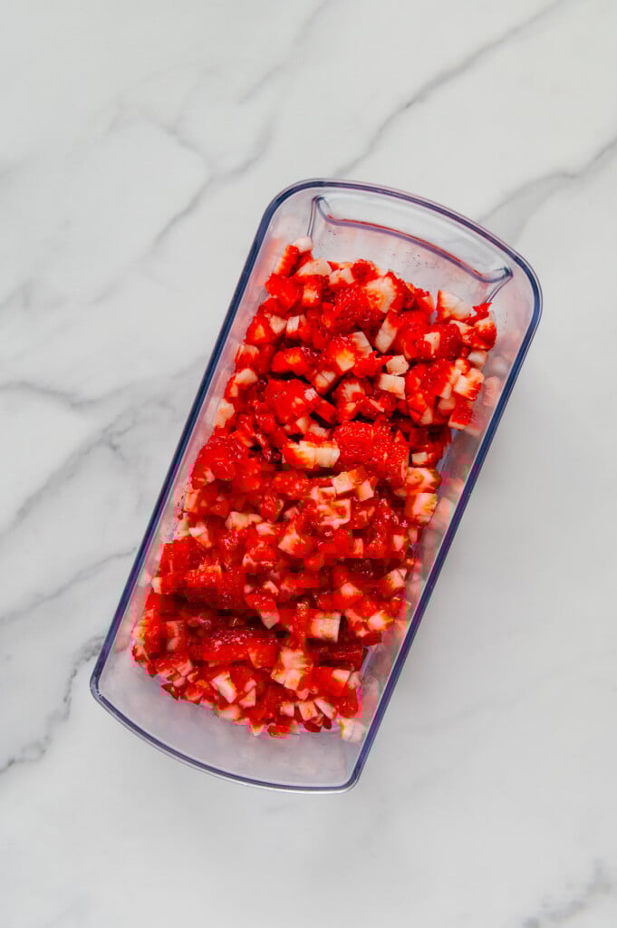 Chopped strawberries in a veggie chopper container with a white marble background.