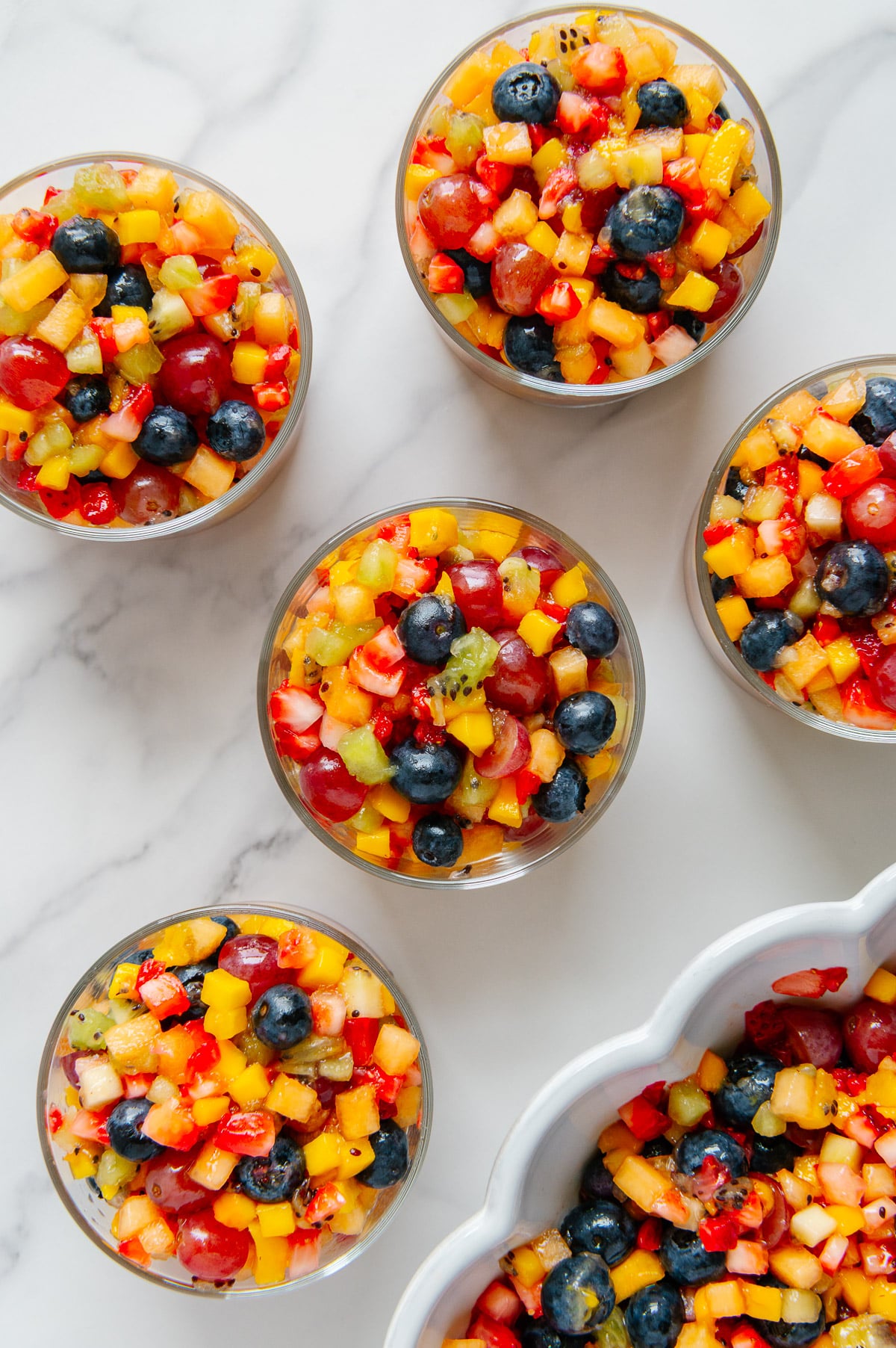 Fresh chopped mixed fruit served in small glass bowls with a white marble background.