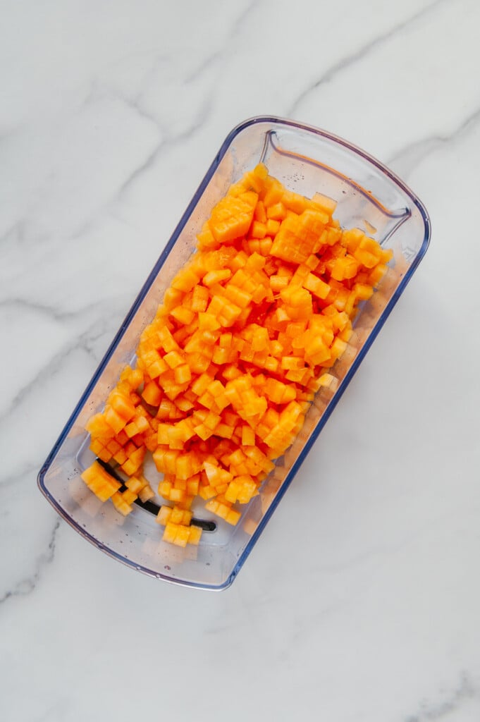 Chopped cantaloupe in a veggie chopper container with a white marble background.