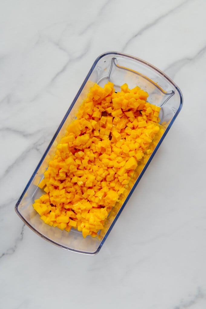 Chopped mango in a veggie chopper container with a white marble background.
