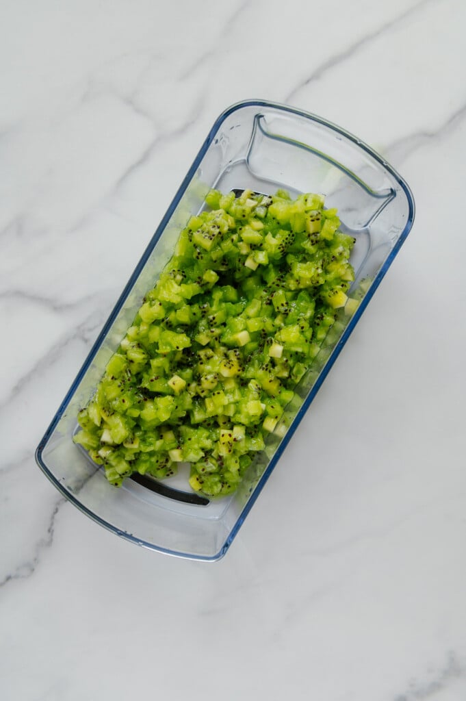 Chopped kiwi in a veggie chopper container with a white marble background.