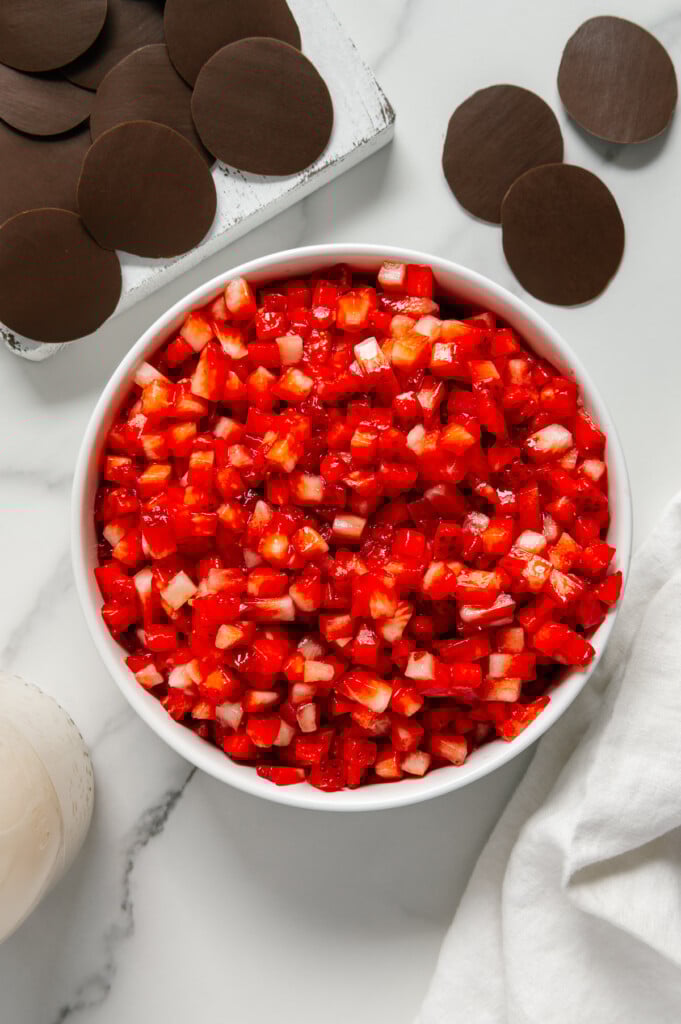 Strawberry "salsa" in a white bowl next to chocolate "chips" with a white marble background.