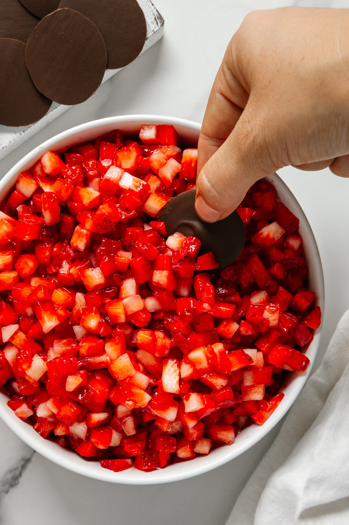 A hand dipping a chocolate "chip" into a bowl of strawberry "salsa."