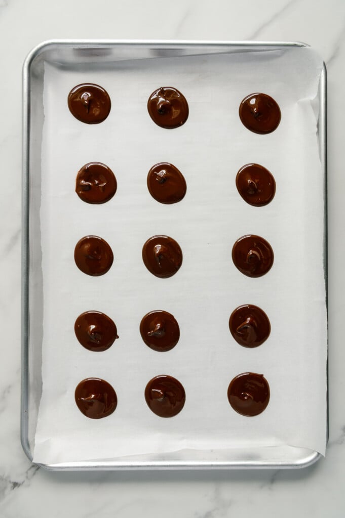 Melted chocolate formed into individual discs on a parchment-lined baking sheet.