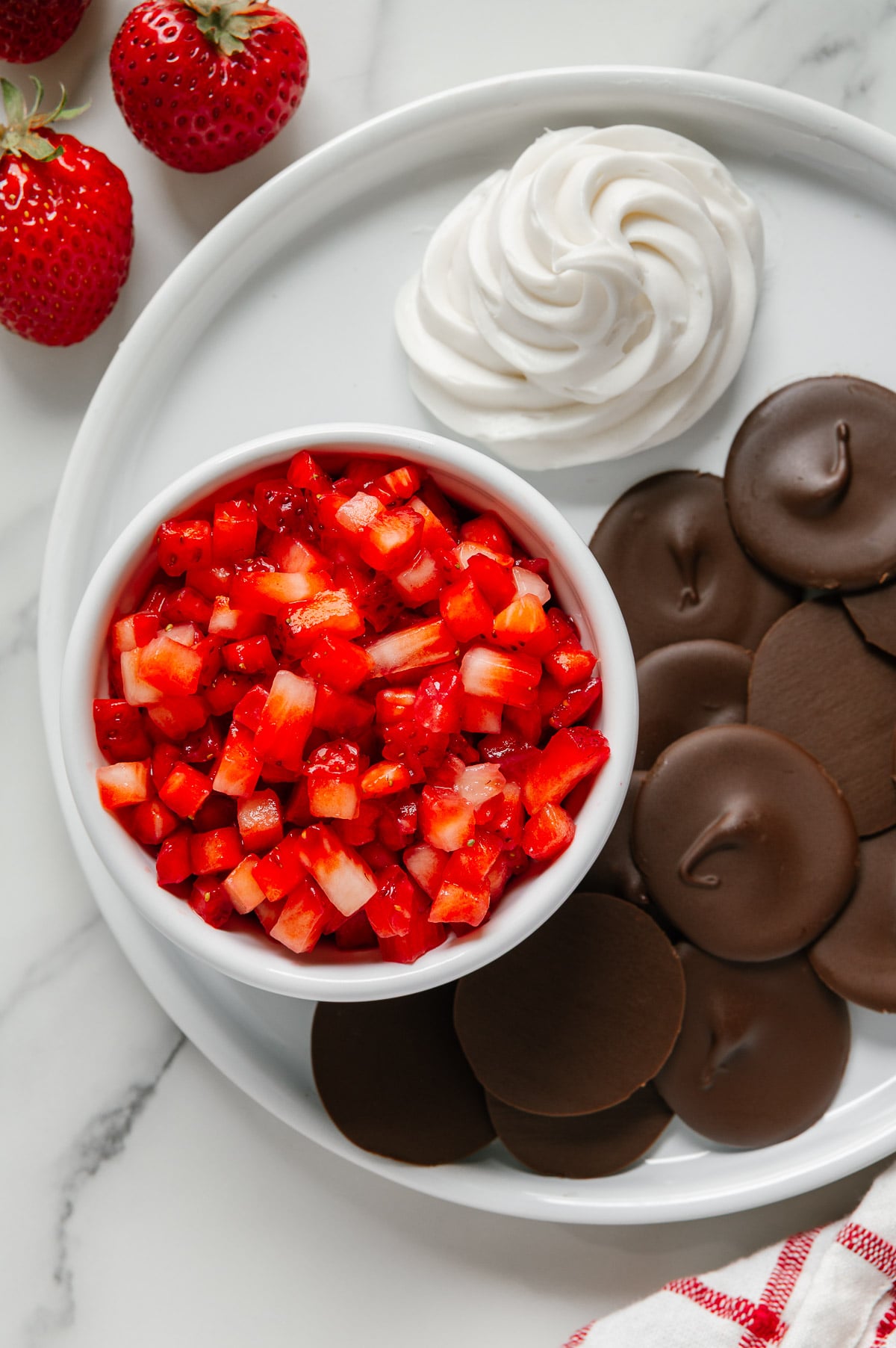 Strawberry "salsa" in a small white bowl on a white plate with chocolate "chips" and coconut whipped cream.