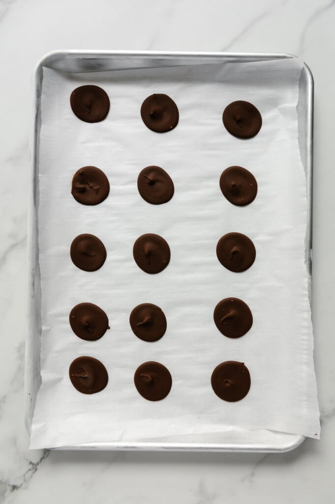 Chocolate formed into individual discs on a parchment-lined baking sheet.