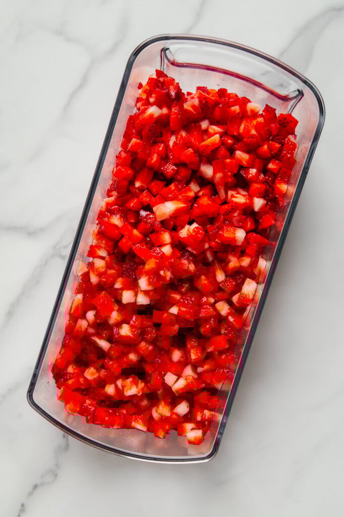 Finely chopped strawberries in the container of a vegetable chopper with a white marble background.