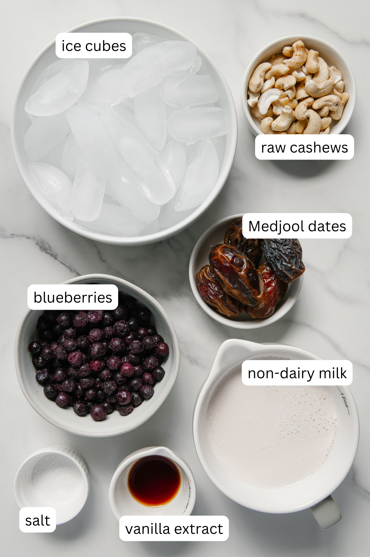 Ingredients of a healthy blueberry milkshake with a white marble background.