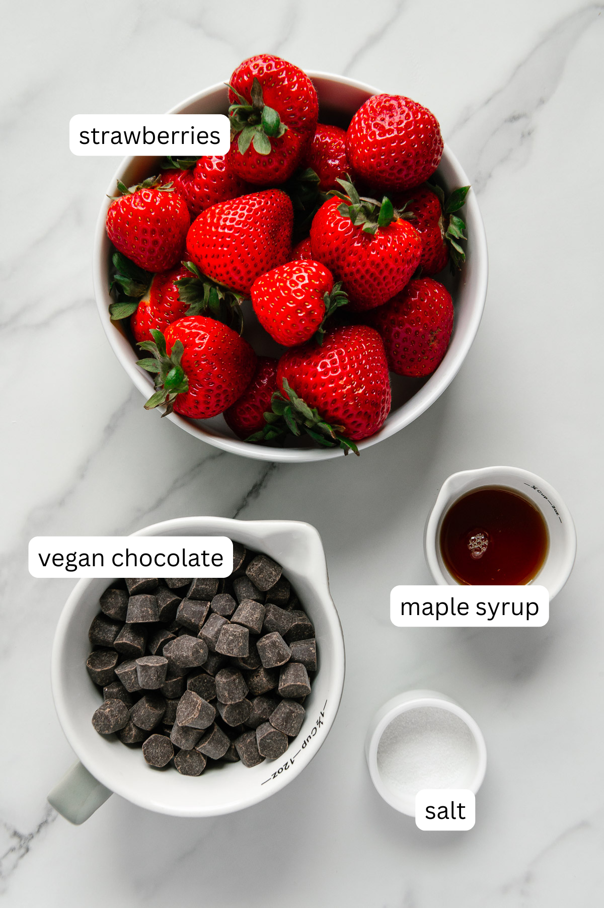 Ingredients of strawberry chocolate chips and salsa with a white marble background.