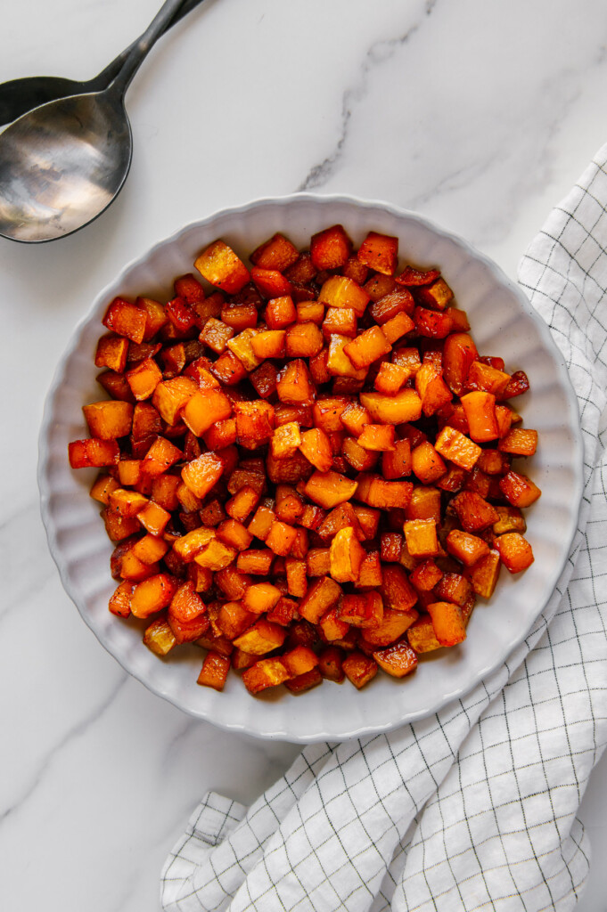 Roasted butternut squash in a white bowl with a white background.