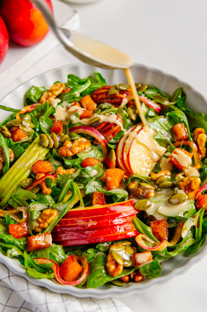 A spoon drizzling tahini over a fall harvest salad.