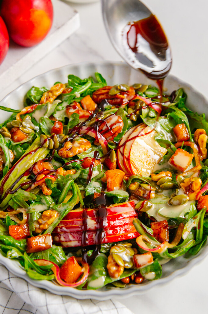 A spoon drizzling date syrup over a fall harvest salad.