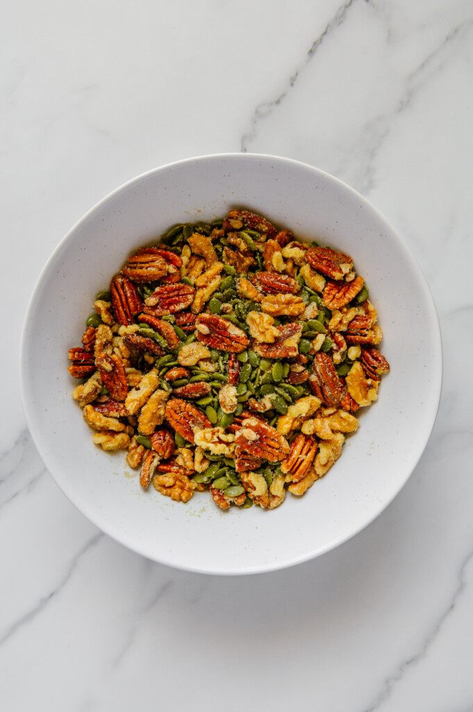 Mixed nuts and seeds in a white bowl with a white marble background.
