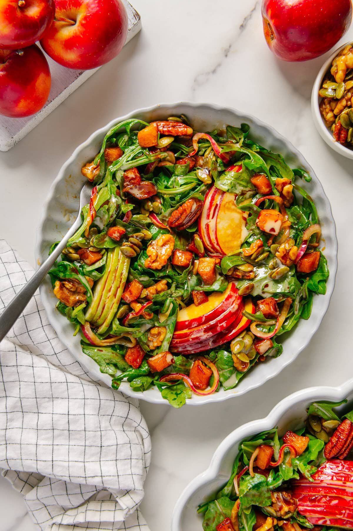 Vegan fall harvest salad in a white bowl served with a fork with a white marble background.