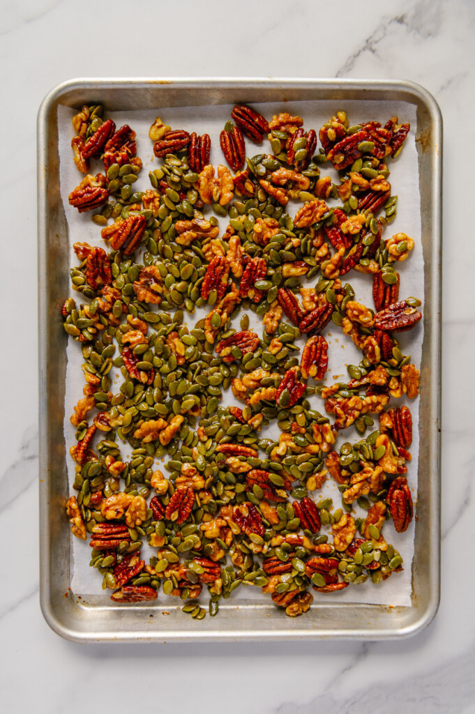 Candied nuts and seeds on a baking sheet with a white marble background.