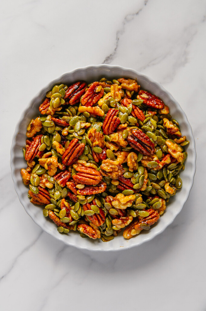 Candied nuts and seeds in a white bowl with a white marble background.