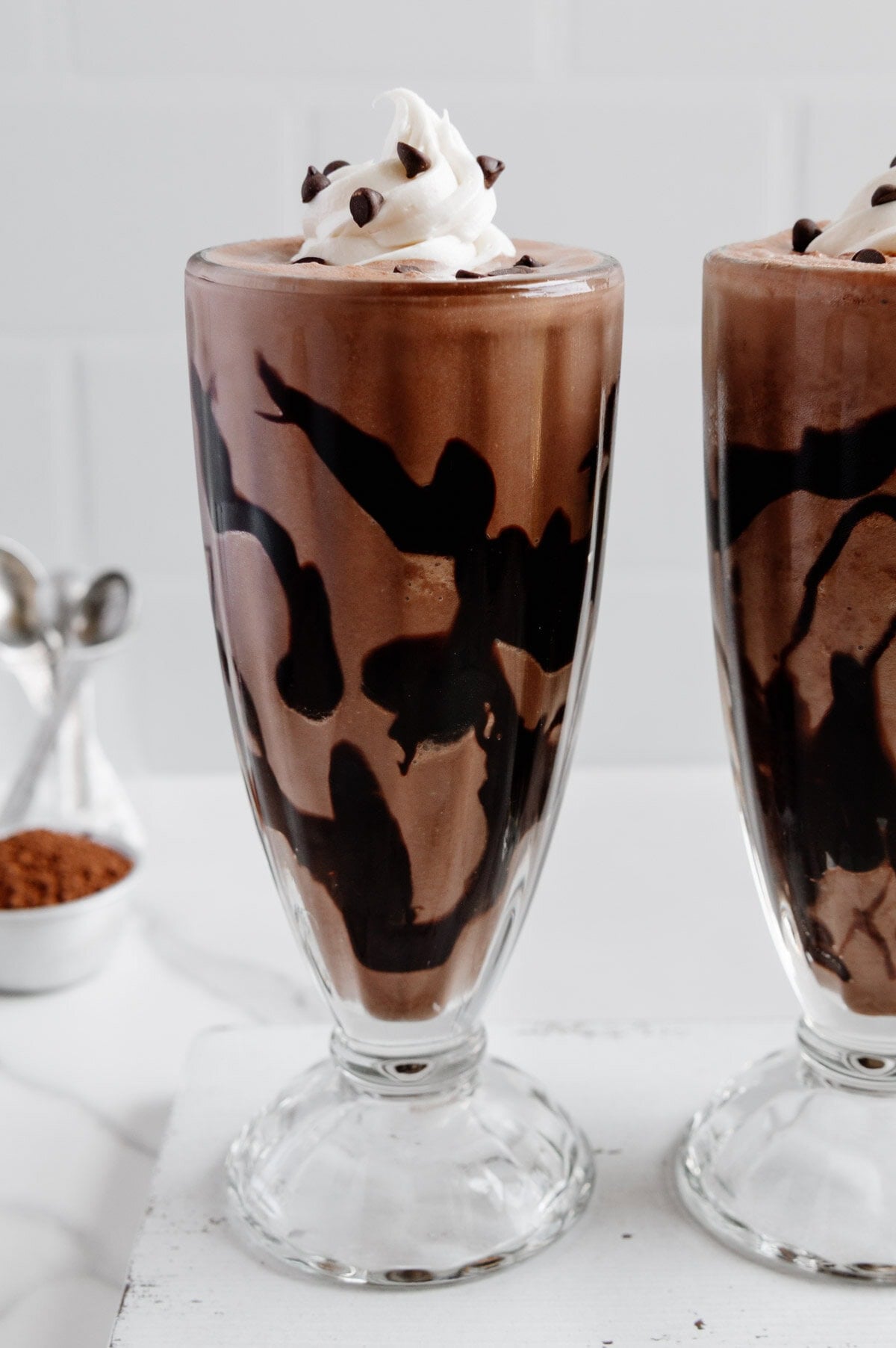 Healthy Chocolate Milkshake Recipe in milkshake glasses with whipped cream and chocolate chips on white background