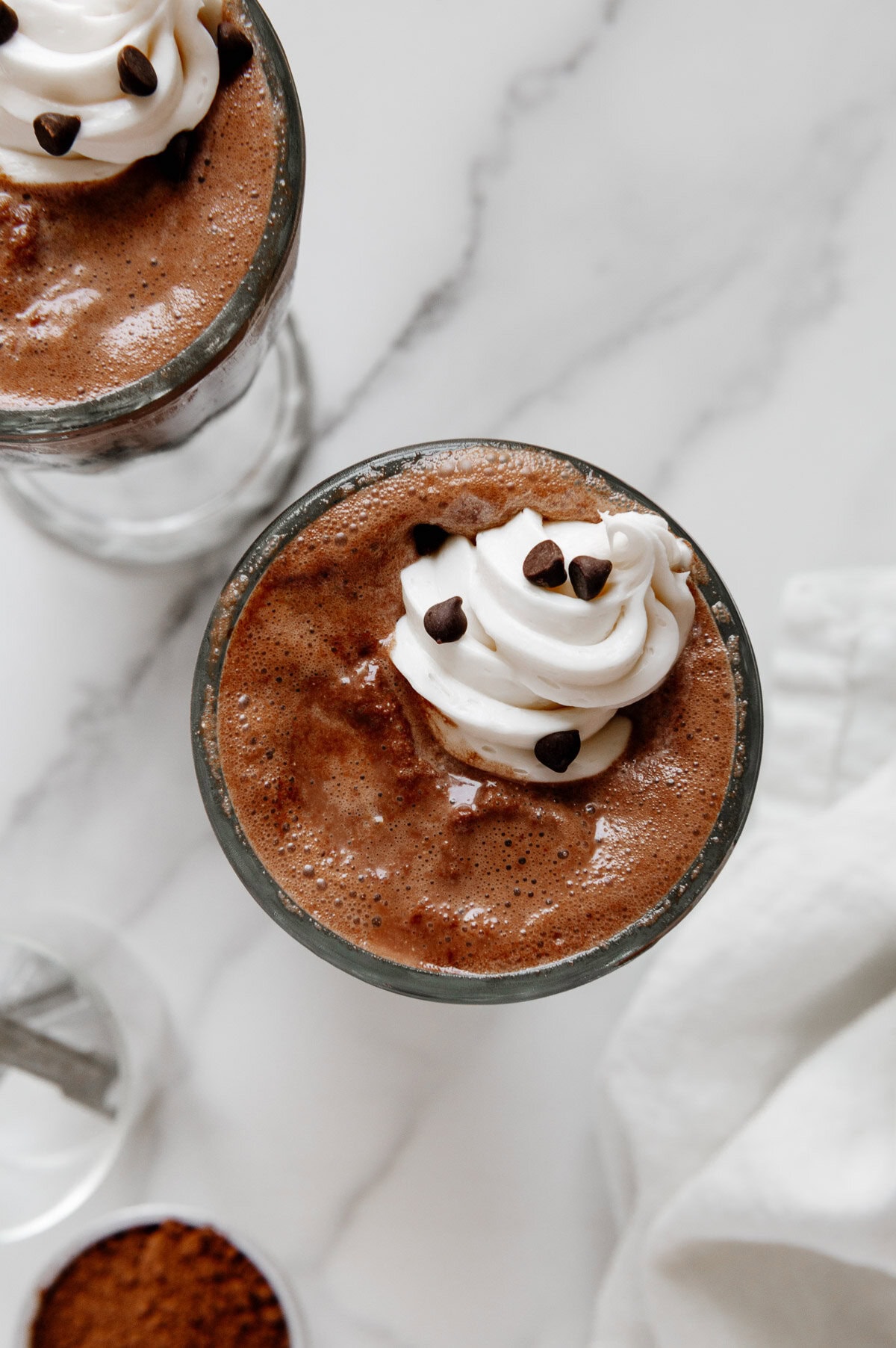 Overhead angle of vegan chocolate milkshakes in tall glasses topped with vegan whipped cream and mini chocolate chips.