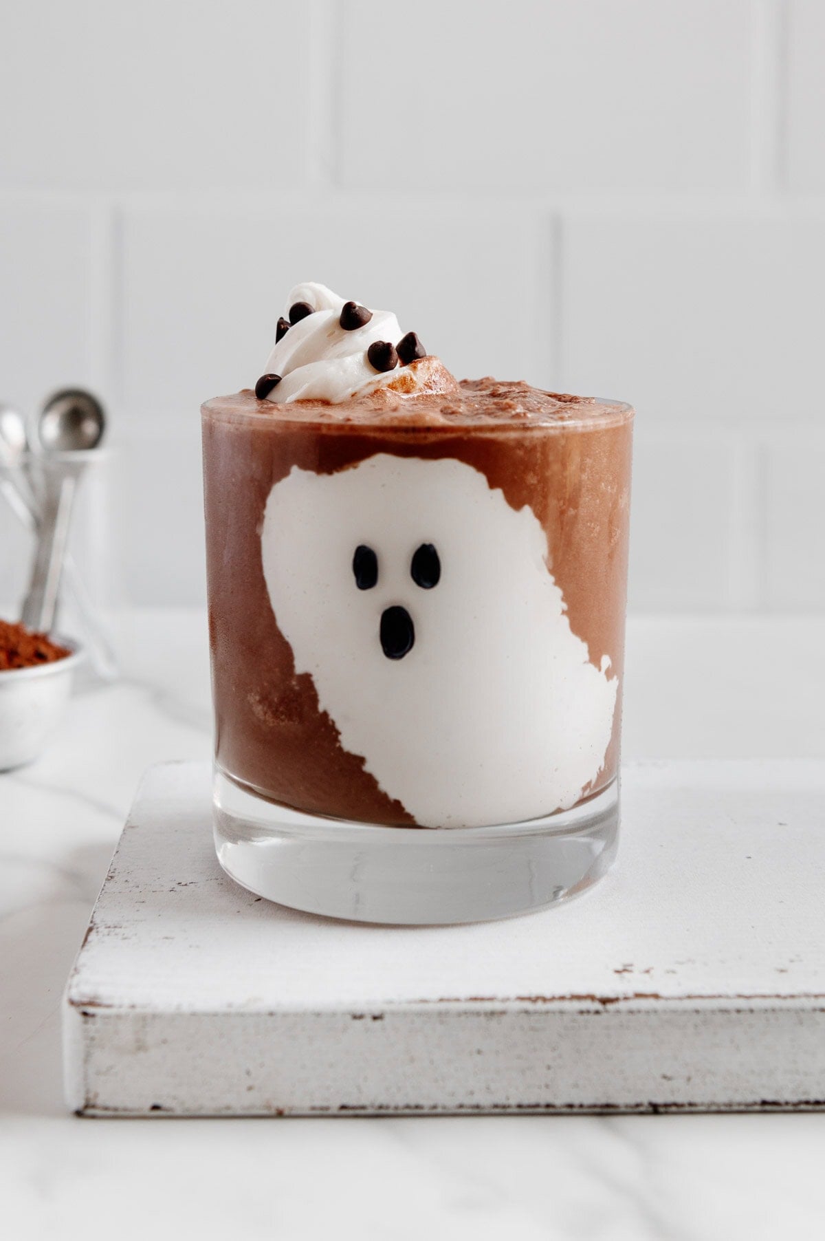 A vegan chocolate milkshake in a glass with marshmallow fluff on the inside to look like a ghost on the side of the glass.