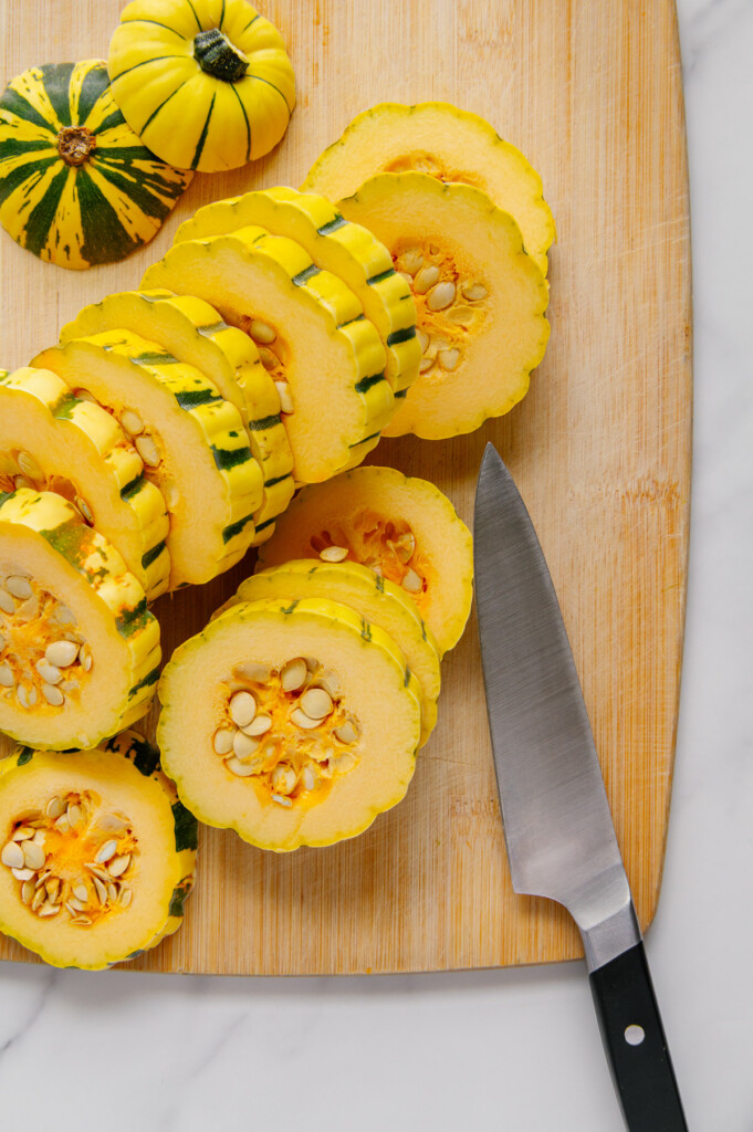 Delicata squash sliced into rings on a wooden cutting board next to a sharp knife.