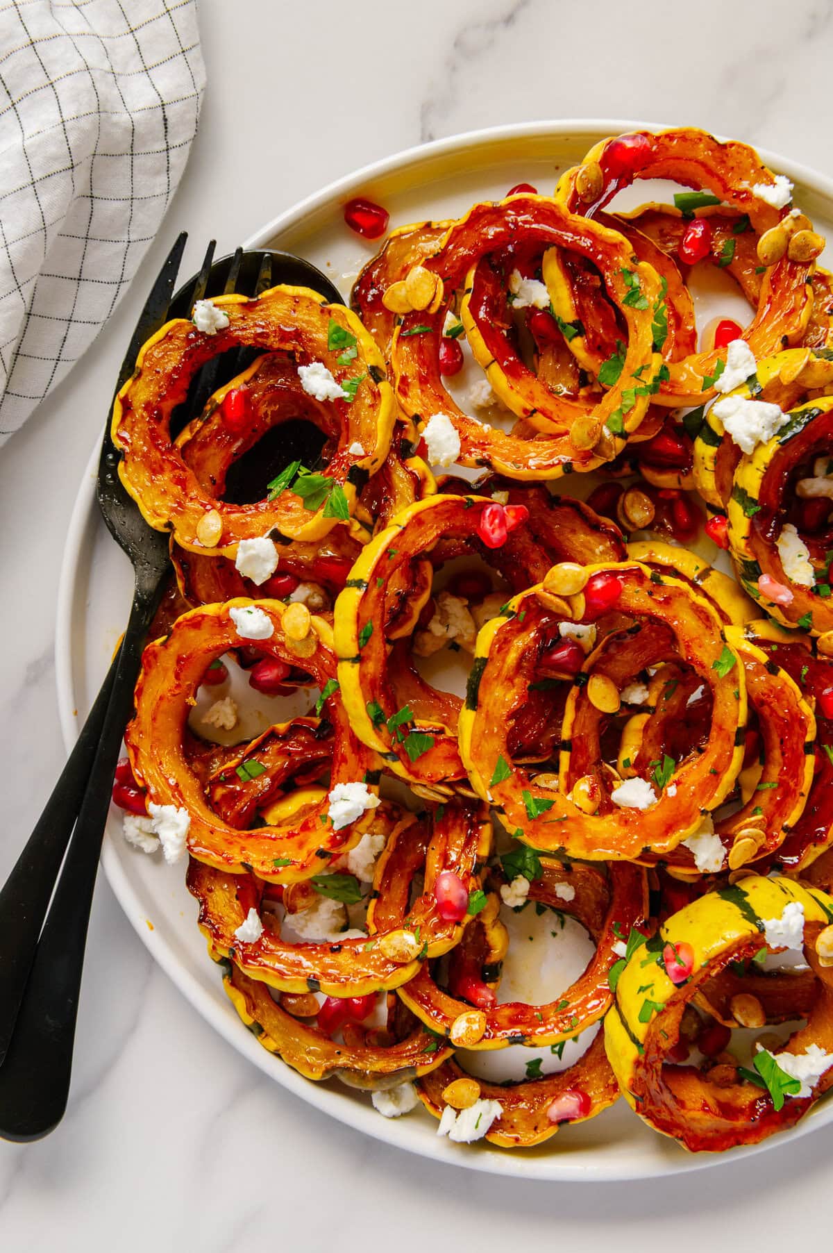 A plate full of roasted delicata squash garnished with vegan goat cheese, pomegranate seeds and fresh parsley.