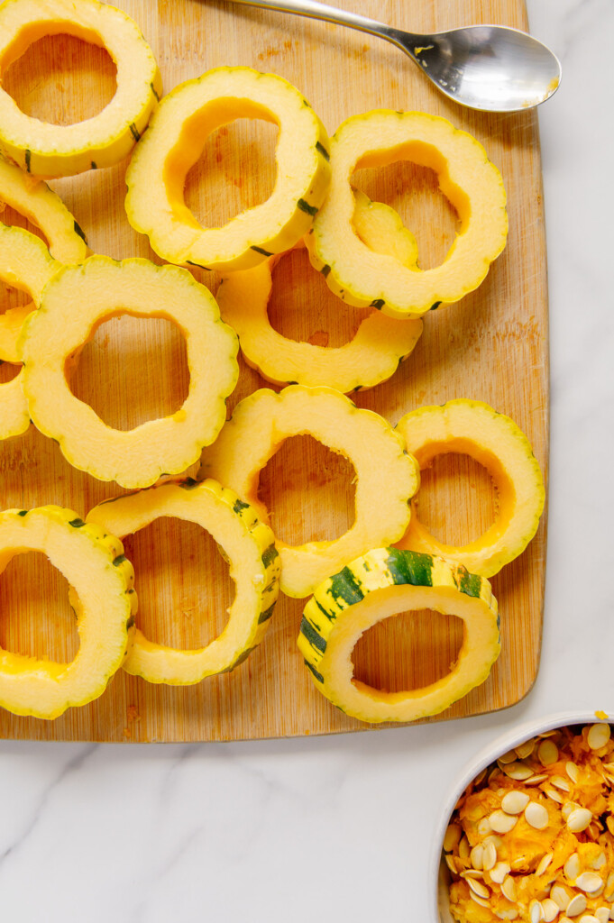 Rings of delicata squash with the seeds removed on a wooden cutting board.