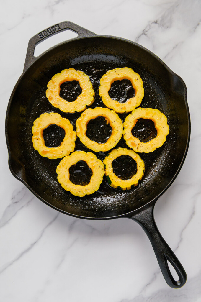 Slices of delicata squash on a cast iron skillet.
