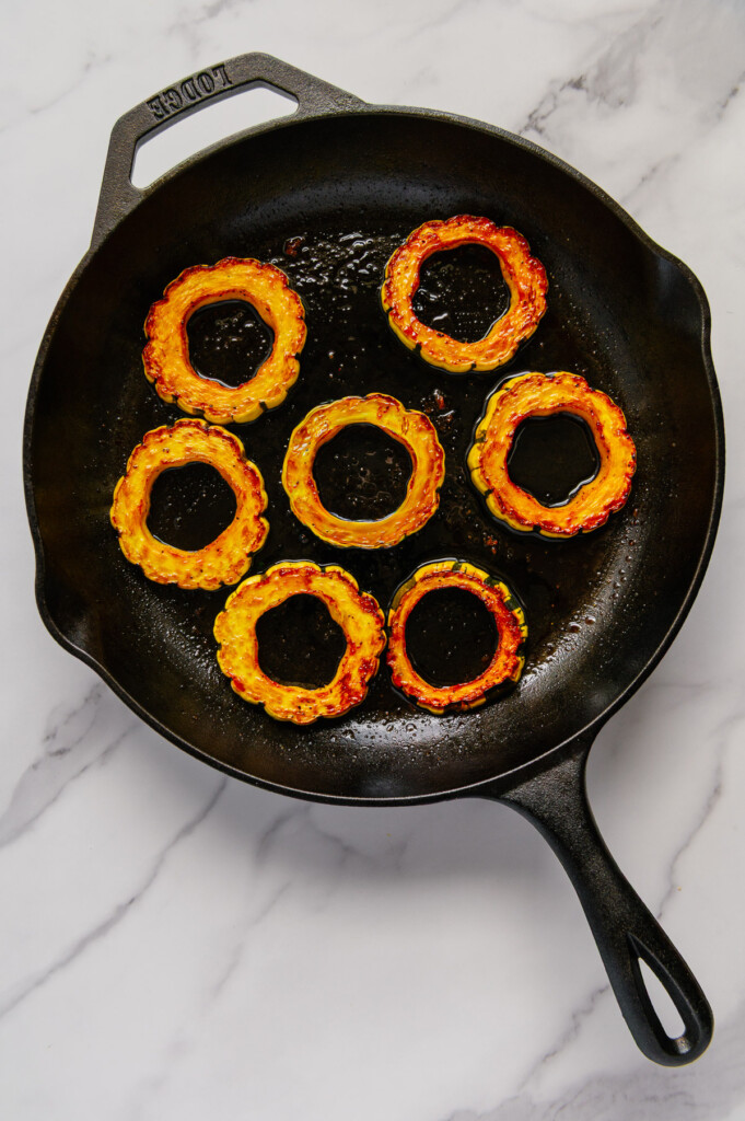 Roasted delicata squash in a cast iron skillet with a white marble background.