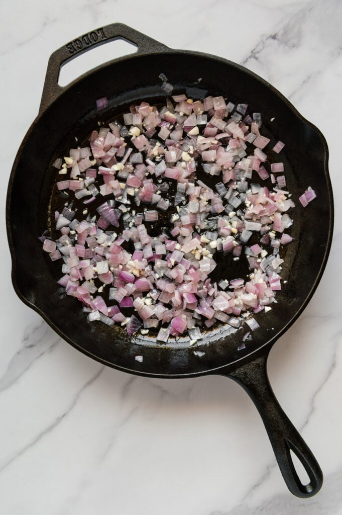 Sautéed onions and garlic in a cast iron skillet with a white marble background.