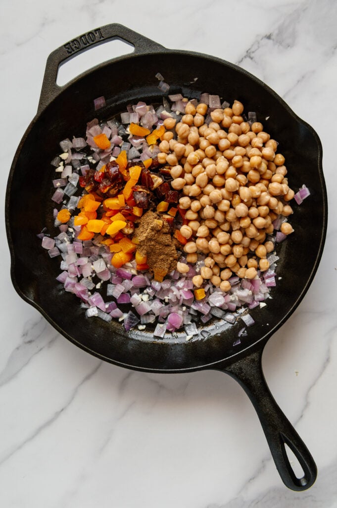 Moroccan stew ingredients in a cast iron skillet with a white marble background.
