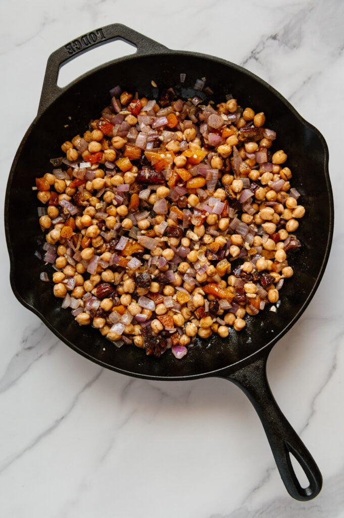 Sautéed chickpeas and other ingredients in a cast iron skillet with a white marble background.