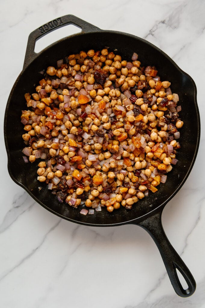 Moroccan chickpea stew in a cast iron skillet prior to adding the tomatoes with a white marble background.