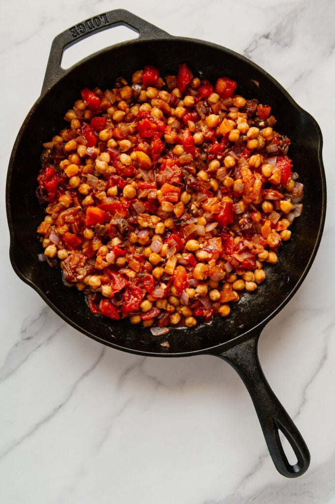 Moroccan chickpea stew in a cast iron skillet prior to being covered and boiled with a white marble background.