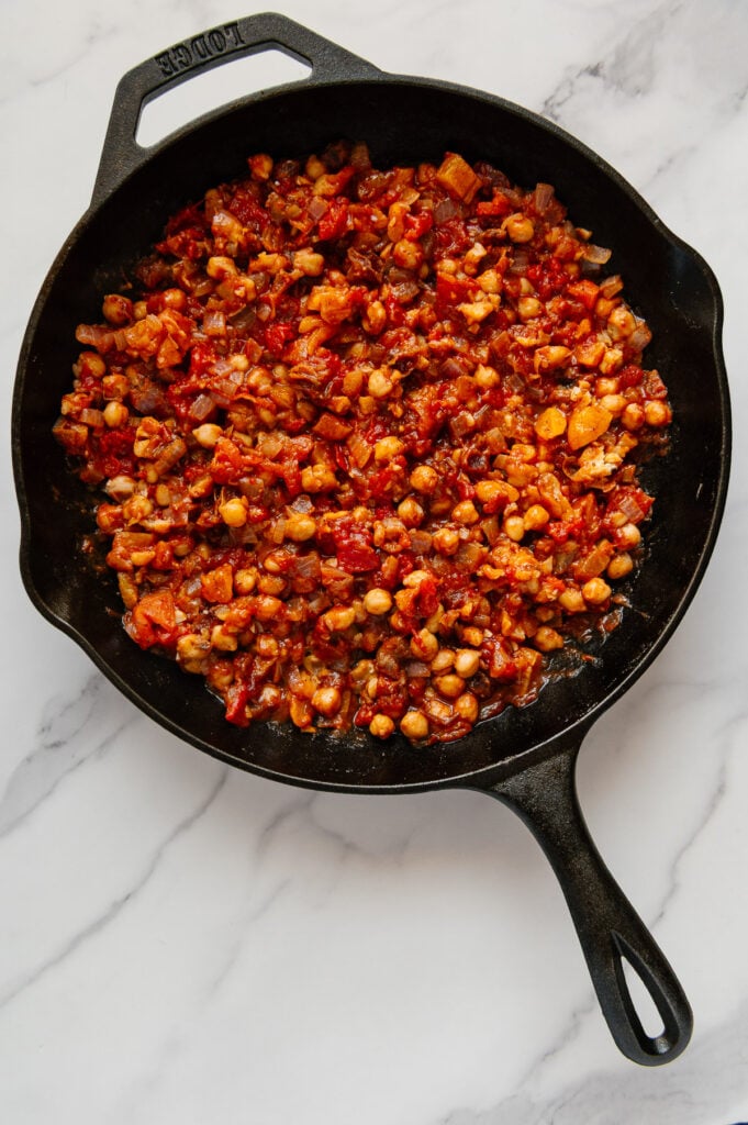 Moroccan chickpeas in a cast iron skillet with a white marble background.
