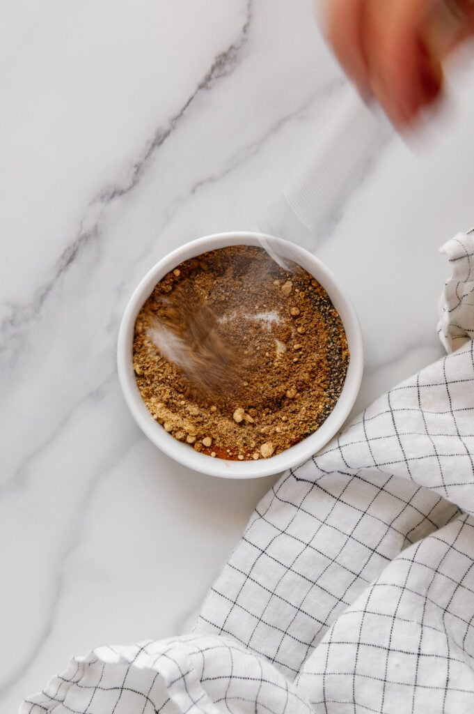 Using a whisk to mix spices into a ras el hanout spice blend.