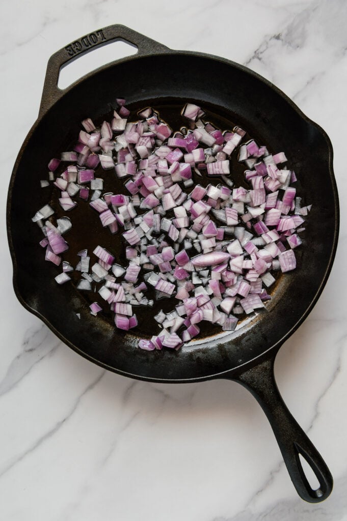 Diced red onions in a cast iron skillet with a white marble background.