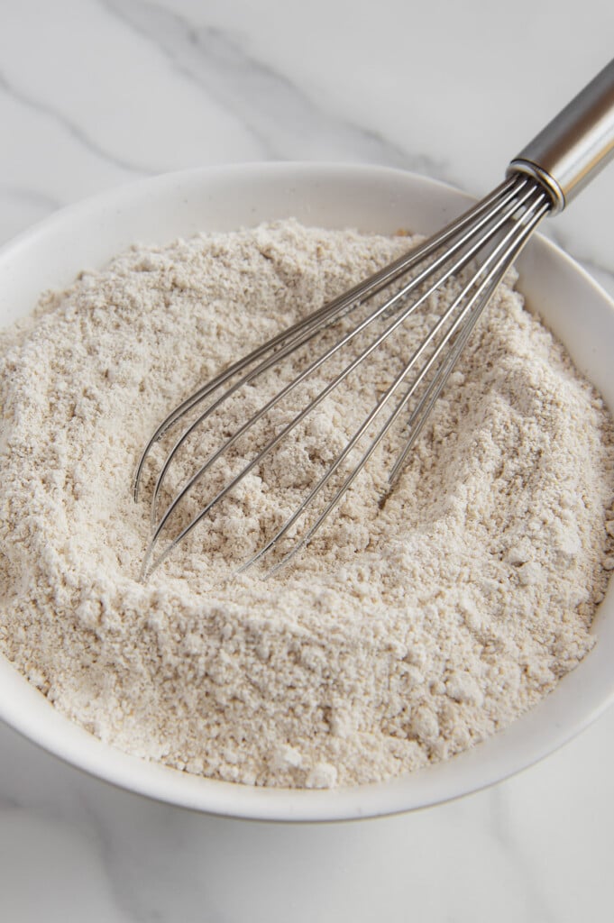A whisk in a white bowl of oat flour.