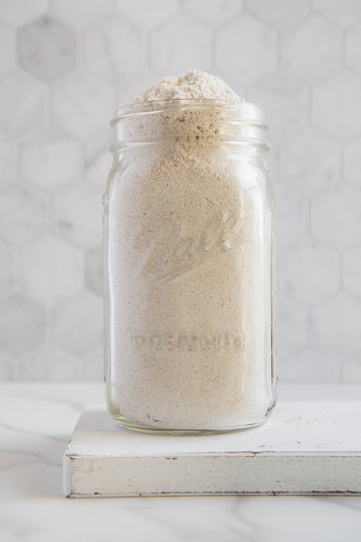 Homemade oat flour in a large glass jar with a white background.