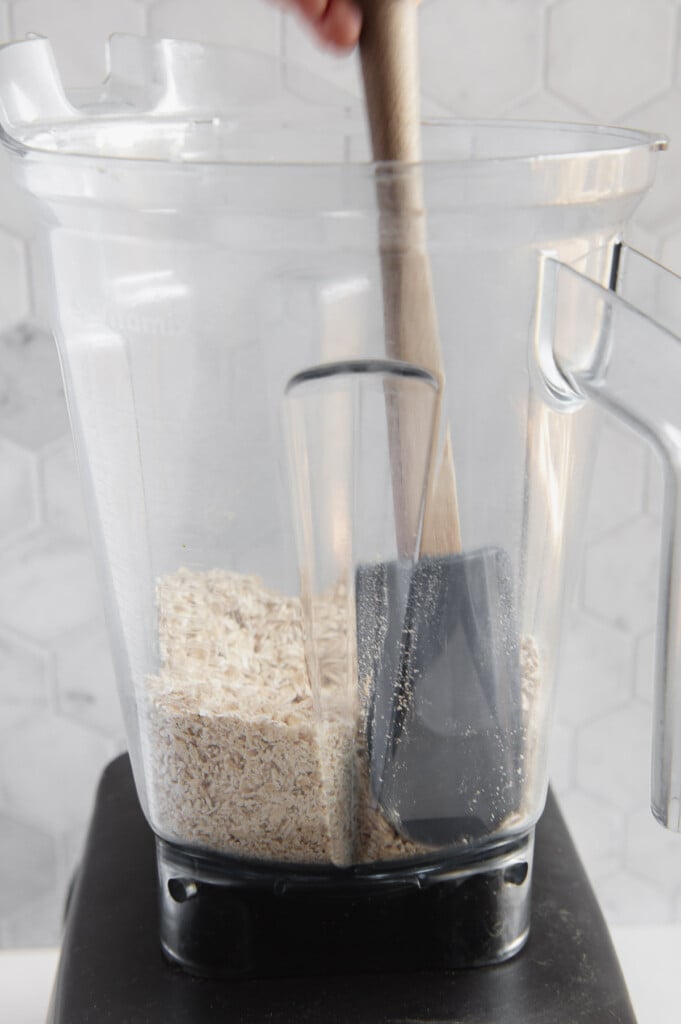 A gray spatula in a blender filled with oats.