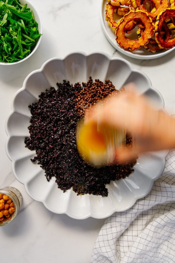 Pouring dressing overtop lentils and forbidden rice in a white serving plate.
