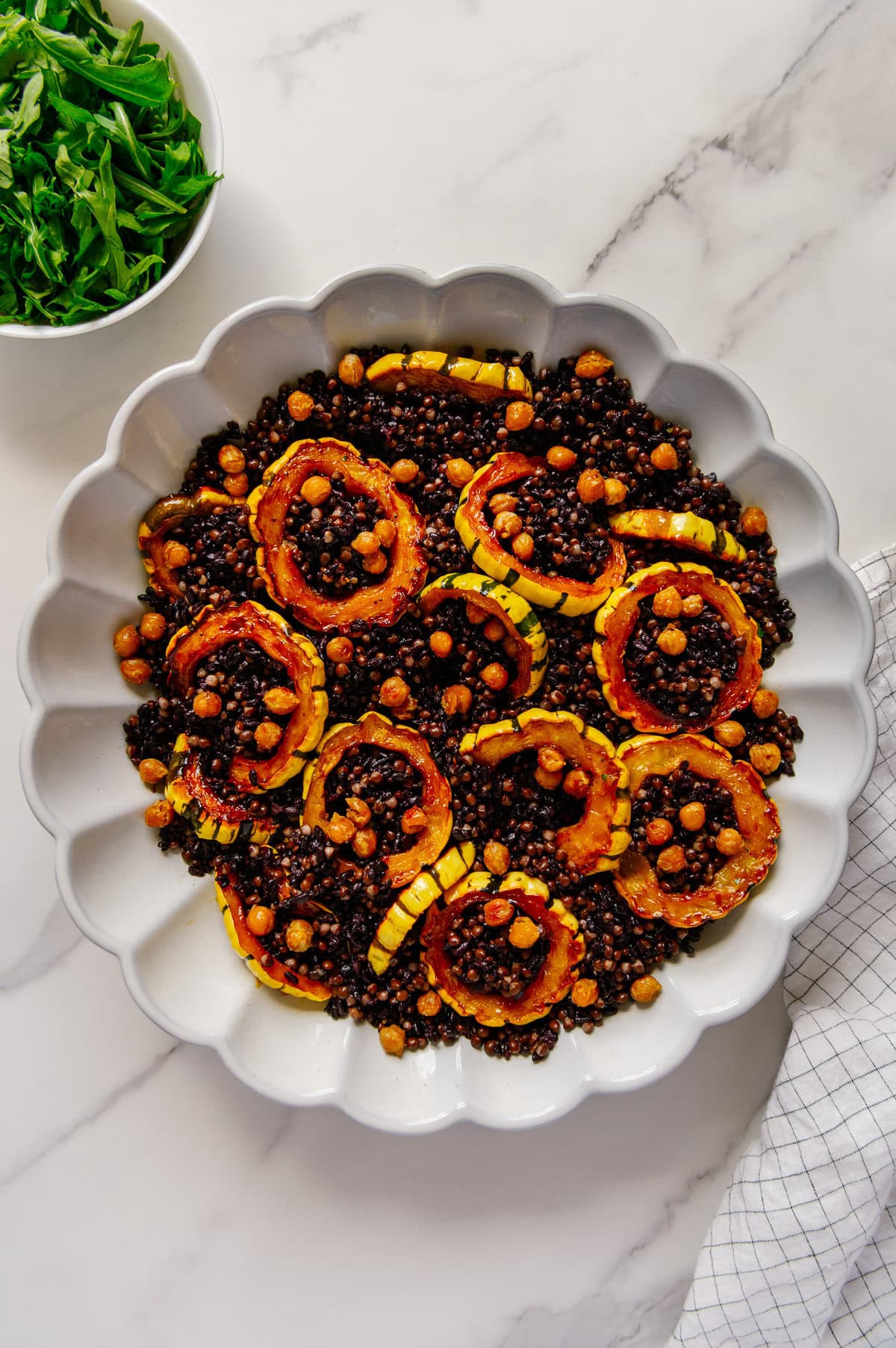 Delicata squash rings nestled in a bed of black lentils and forbidden rice in a white serving plate with crispy chickpeas overtop.