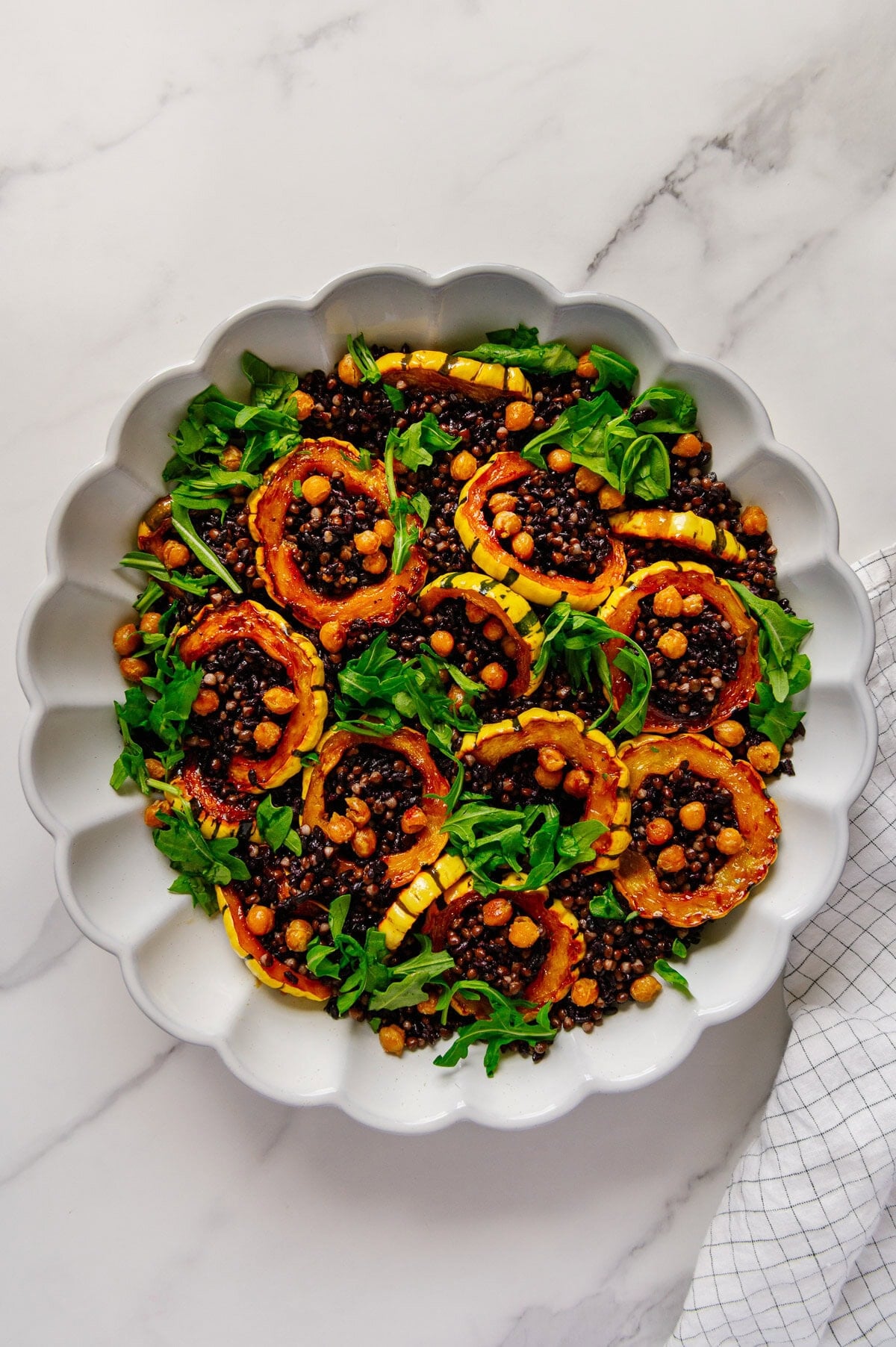 Delicata squash rings and crispy chickpeas nestled in a bed of black lentils and forbidden rice topped with chopped arugula in a white serving plate.