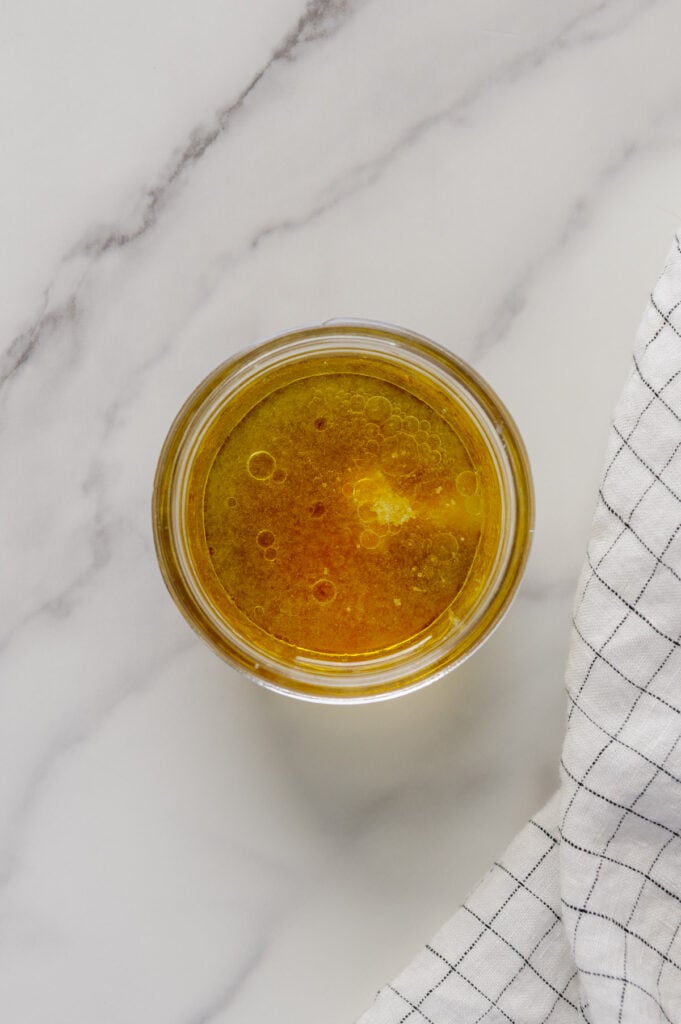 Maple lemon dressing ingredients in a small glass bowl with a white marble background.
