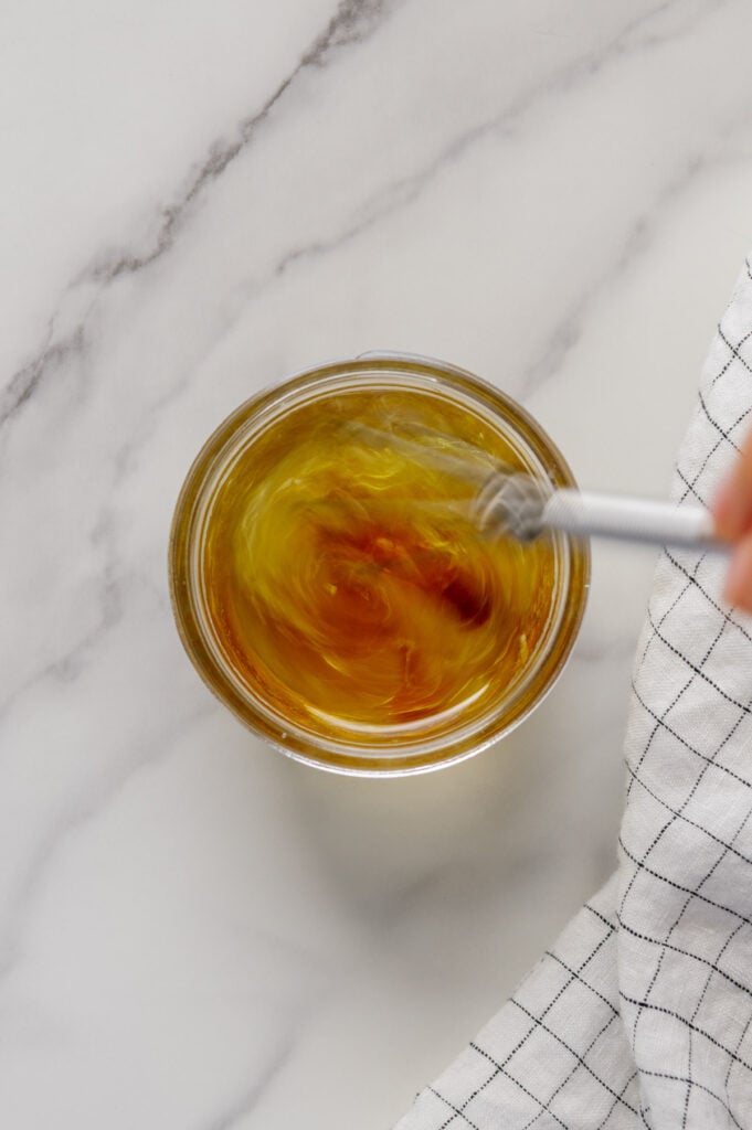 Using a spoon to whisk dressing ingredients in a small glass bowl.