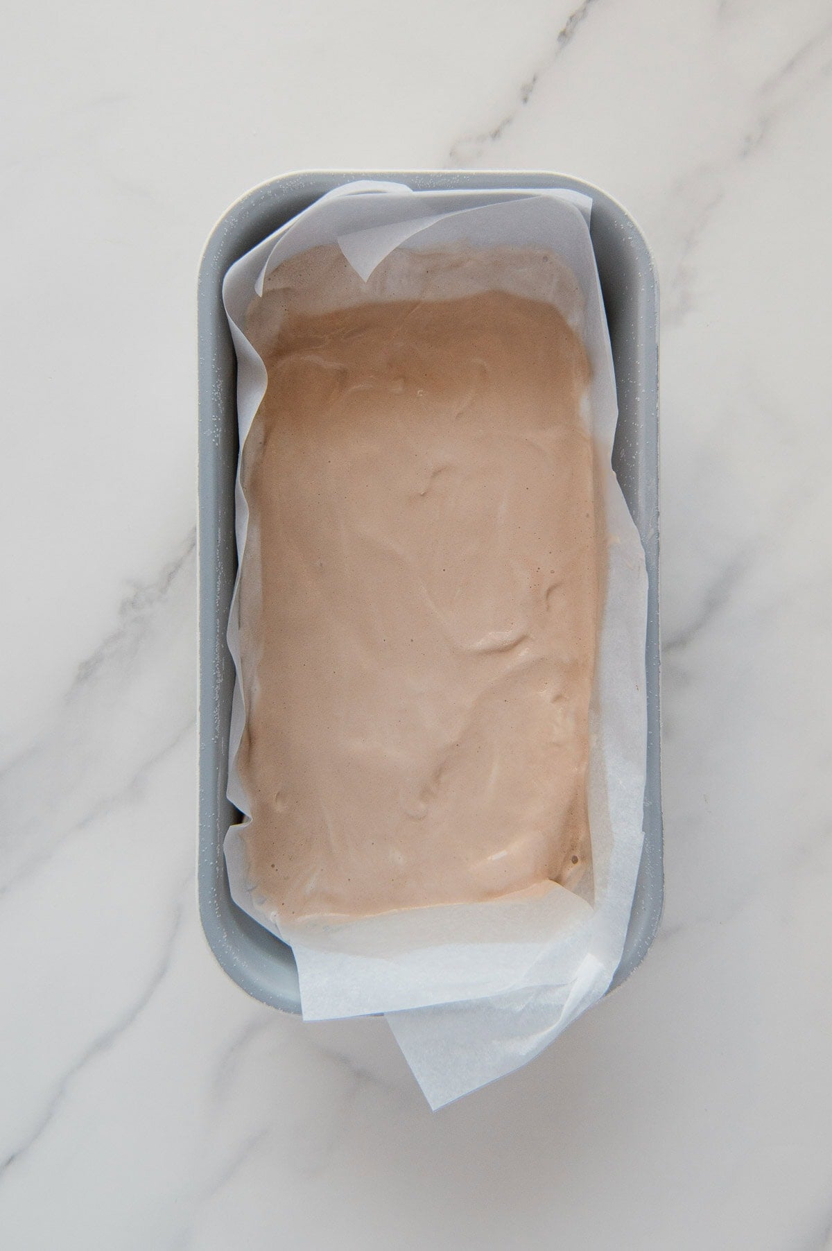 Frozen vegan 3 Musketeers filling in a loaf pan lined with parchment paper.