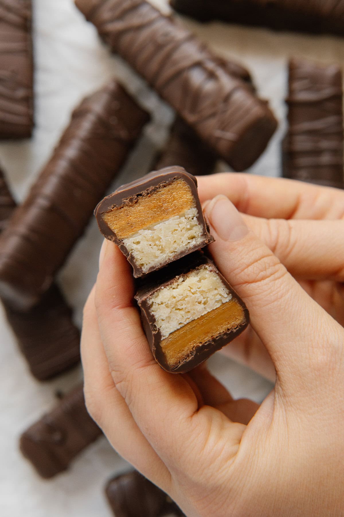 Two hands holding two halves of a homemade Twix bar showing the filling.