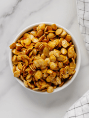 Roasted winter squash seeds in a white bowl with a white marble background.