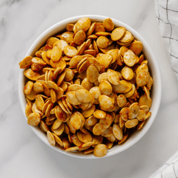 Roasted winter squash seeds in a white bowl with a white marble background.
